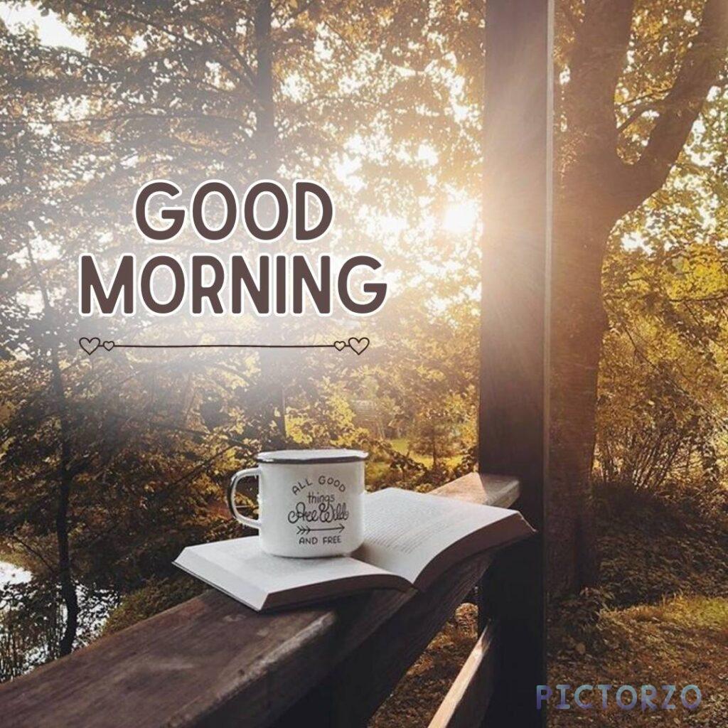 A cup of coffee sitting on top of a book on a wooden railing, with the text GOOD MORNING overlaid on top of the image
