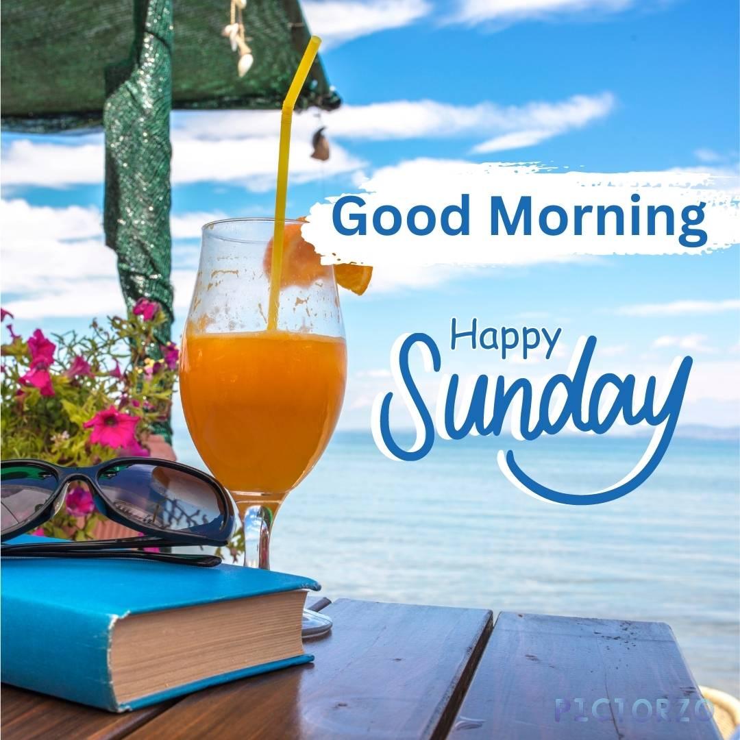 Good Morning Images Sunday 1 A glass of orange juice, sunglasses, and a book on a wooden table at the beach on a sunny Sunday morning. The table is set up under a palm tree, and the ocean is visible in the background. The sand is white and the sky is blue.