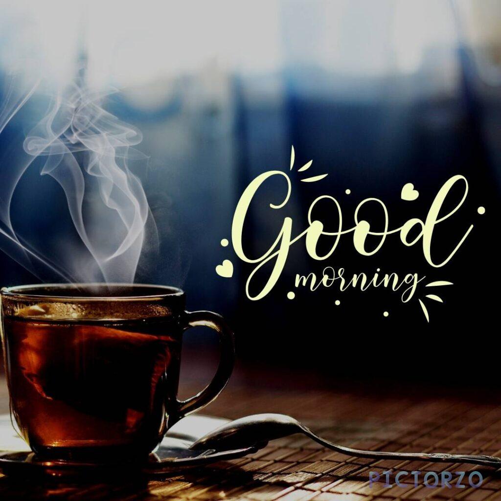 A steaming cup of tea with a slice of lemon on a wooden table. The text Good morning is written in cursive font above the cup of tea.