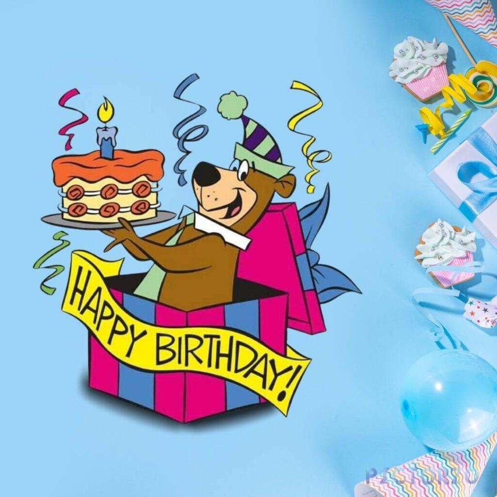 A cheerful Yogi Bear holding a birthday cake decorated with a single lit candle in a gift box with blue wrapping paper and a yellow ribbon, against a light blue background. The text "HAPPY BIRTHDAY!" is written in yellow letters above the cake.