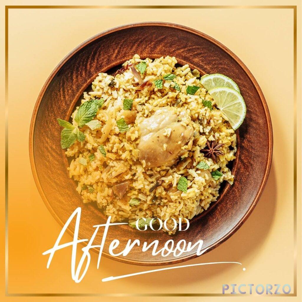 A close-up photo of a plate of chicken biryani with rice and vegetables on a table. The plate is decorated with a sprig of cilantro and a slice of lemon. The text "Good Afternoon" is written in the top left corner of the image.