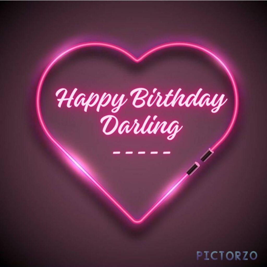 A glowing pink neon sign in the shape of a heart with the words Happy Birthday darling written on it inside. The sign is casting a soft pink glow on the surrounding area.