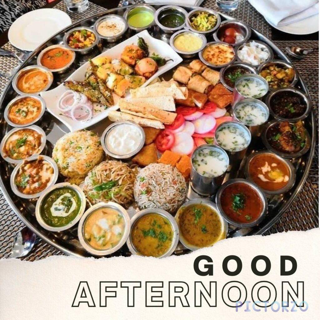 A good afternoon lunch image of a large Indian thali meal on a round metal tray. The thali includes a variety of vegetarian dishes, such as rice, dal, naan bread, and various curries. The text "GOOD AFTERNOON" is written in the center of the tray.