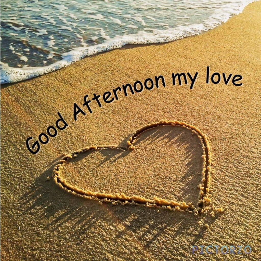 A heart drawn in the sand on a beach with the text Good afternoon my love. The image is taken during sunset, and the sky is a beautiful shade of orange.