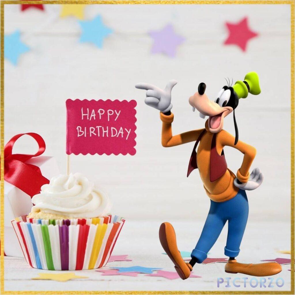 A jubilant Goofy, a cartoon character from Walt Disney, stands beside a giant cupcake decorated with a Happy Birthday sign. He is wearing a festive party hat and has a big smile on his face