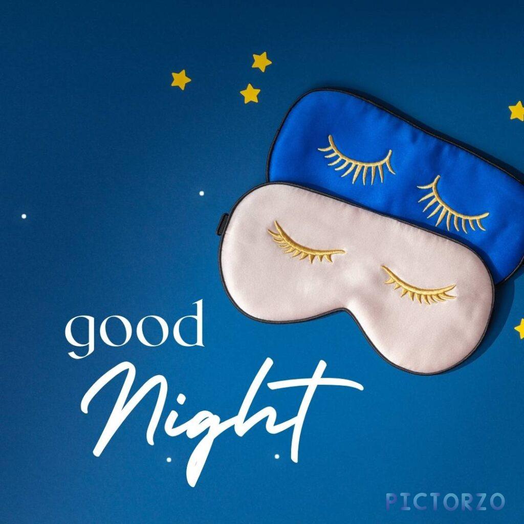 A pair of black silk sleep masks with closed eyes and the text good Night embroidered on them. The sleep masks are resting on a white background