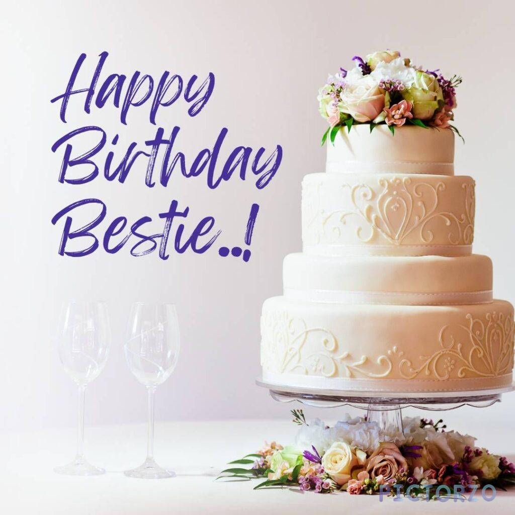 A photo of a two-tier cake decorated with white frosting and colorful sprinkles. The top tier of the cake has a pink fondant plaque that reads "Happy Birthday Bestie! The bottom tier is decorated with pink and purple rosettes made of frosting. 