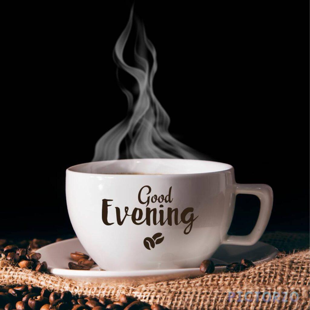 A steaming cup of coffee with the text "Good Evening" in the background. The coffee is in a white mug with a brown handle, and it is sitting on a dark wooden table. There is a small spoon next to the mug.