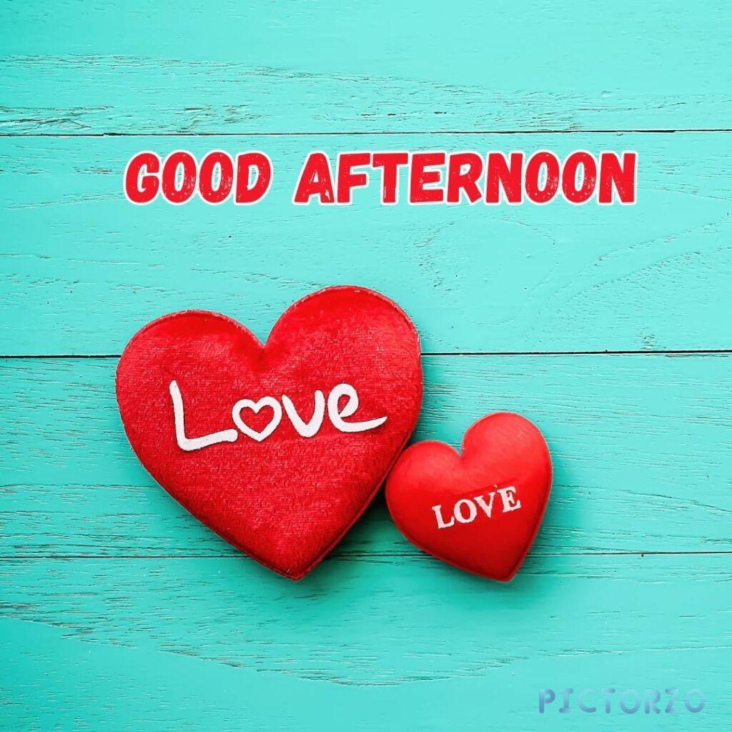 Two red hearts on a blue wooden table with the text Good afternoon, love