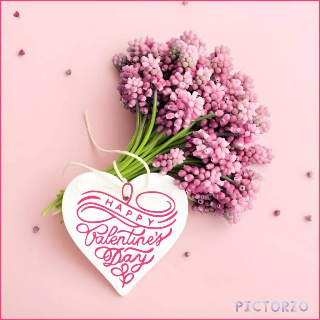 A photo of a bouquet of pink roses sitting next to a white heart-shaped card. The card has red text that reads Happy Valentine's Day