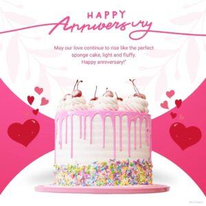 A pink frosted cake, likely red velvet cake, with a single cherry on top. The cake is displayed on a plate & has the message Happy Anniversary written in white frosting above a decorative swirl design
