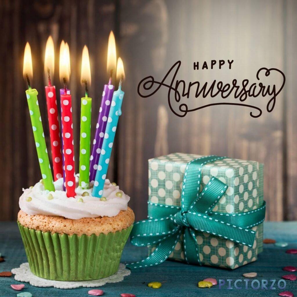 A single cupcake decorated for an anniversary celebration. The cupcake is frosted white and sits on a wooden table. Next to the cupcake is a small, wrapped gift box with a green ribbon.