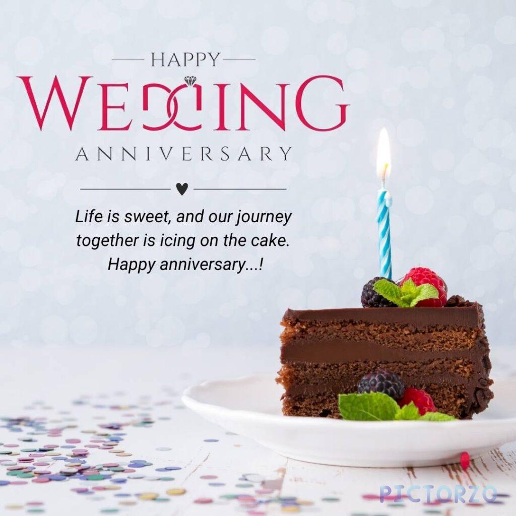 A slice of chocolate cake on a plate decorated with whipped cream, berries and a lit candle. The plate sits on a table with a background message that reads "Happy Wedding Anniversary. Life is sweet and our journey together is icing on the cake. Happy Anniversary!"